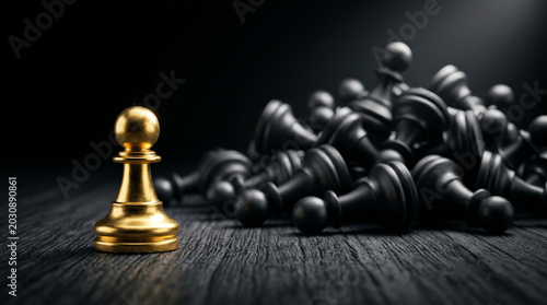 Shiny golden pawn separated from defeated black pieces on wooden texture