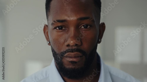 Portrait of serious African American businessman in casual attire stands in office closeup. Man entrepreneur with tranquil facial expression in corporate space