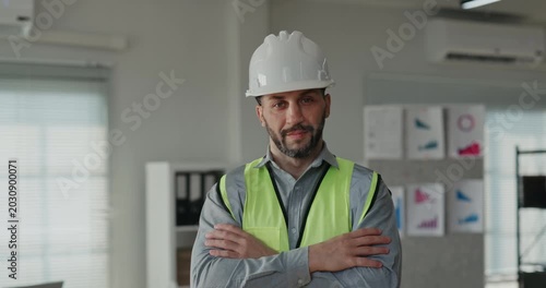 Portrait of Middle Eastern bearded construction manager in hard hat and safety vest in office. Specialist crosses arms and looks at camera with confidence