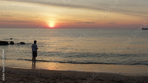 Fotografia Lone fisherman stands in the serene ocean shallows, angling at sunrise for recreation and wellbeing, with the golden light reflecting on the calm sea