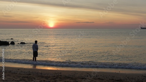 Fotografia Lone fisherman stands in the serene ocean shallows, angling at sunrise for recreation and wellbeing, with the golden light reflecting on the calm sea