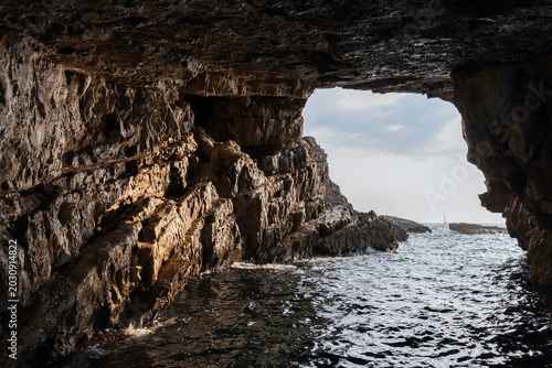 Billede på lærred Dramatic view from the inside of a rocky cave, overlooking the vast sea under a vibrant sky