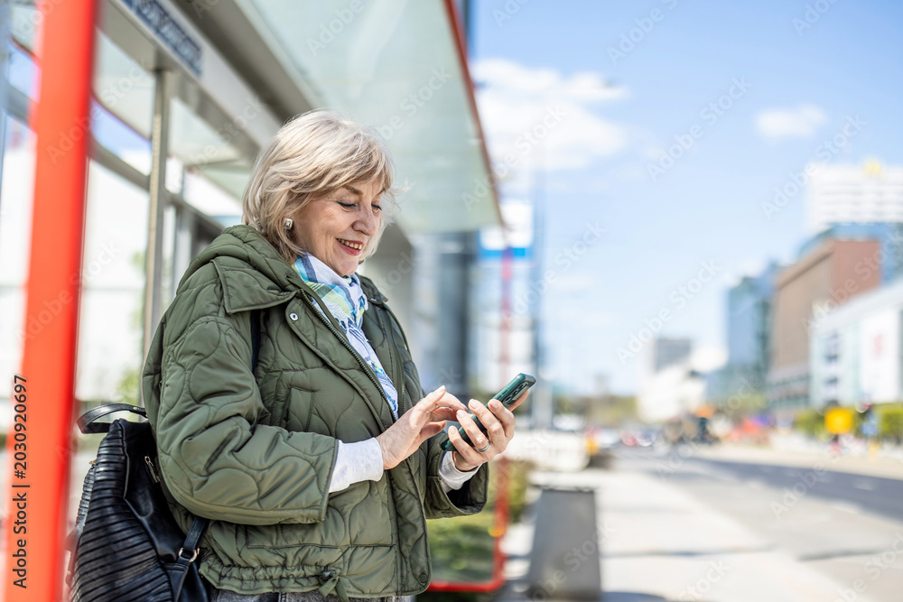 Fototapeta premium Woman using her smartphone while waiting for a bus in the city 