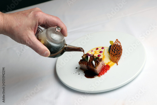Chef Pouring Rich Sauce from Glass Teapot onto Roasted Duck Breast. Fine Dining Gastronomy Plating with Caviar and Tuile on White Plate.
