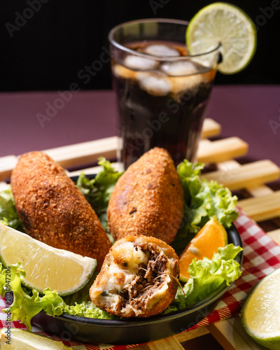 Bild auf Leinwand Crispy Brazilian beef croquettes stuffed with shredded beef and melted cheese, served with lime wedges, lettuce and a soda drink