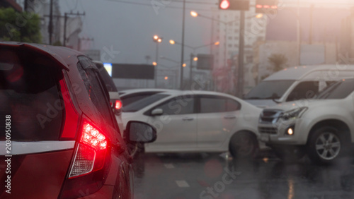 Abstract and blurred of cars are gridlocked on a wet city street during a rainy evening. A red vehicle bright brake light is illuminated in the foreground reflecting off the dark wet road surface.
