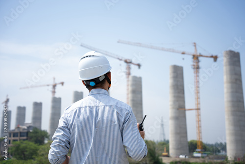 Schilderij op canvas Engineer wearing safety helmet commanding at construction site with cranes and b