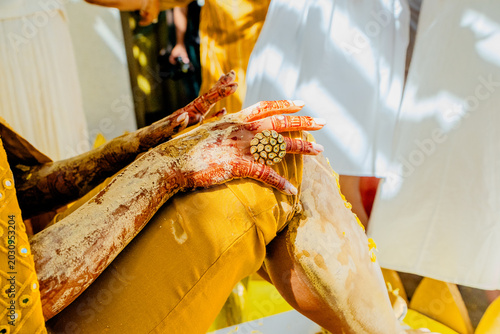 Close up of Indian bride hands with traditional henna mehndi and gold ring during Haldi ceremony. Hindu wedding ritual details, traditional yellow dress.