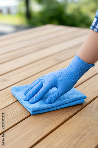 Gloved hand cleans wooden surface with blue microfiber cloth outdoor setting