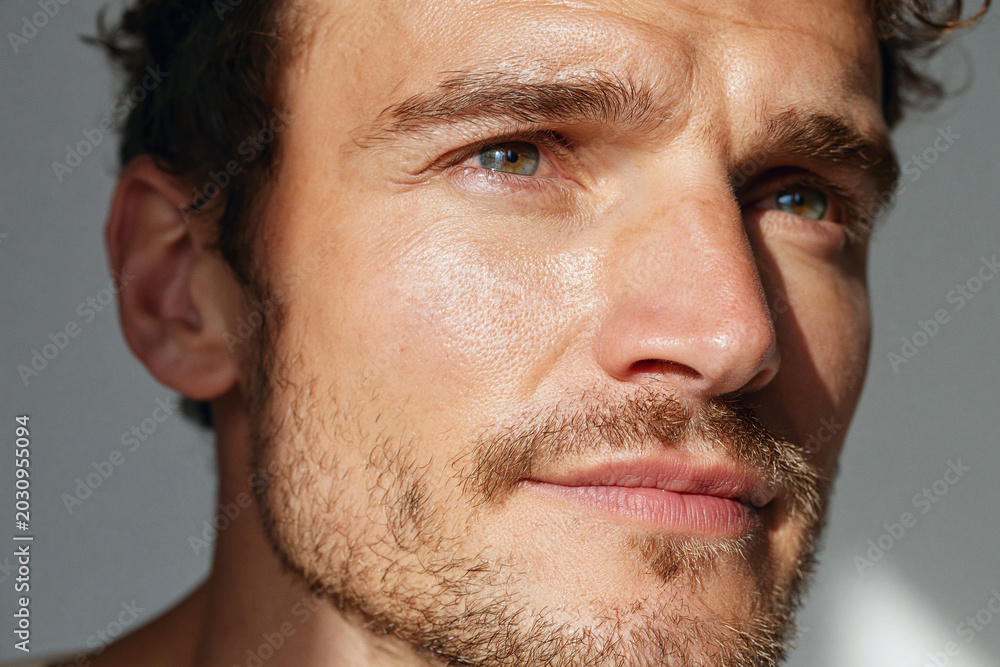 Obraz premium Young man portrait sunlight on cheekbone and jaw, green eyes, short beard, natural skin texture, thoughtful expression