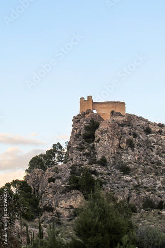 Medieval castle ruins standing on top of a steep rocky hill against a clear evening sky in Cieza.