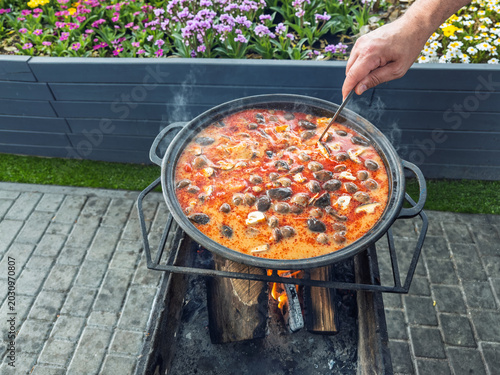 Fotografi Traditional Thai Tom Yum soup cooking in a large kazan over an open fire outdoor
