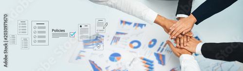 Obraz na płótnie A group of diverse professionals demonstrating teamwork and collaboration by placing their hands together over business charts and policy documents, symbolizing unity and strategic planning