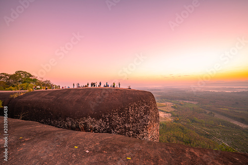 Photography Epic sunrise at a famous Thai viewpoint, capturing tiny human figures on a colossal rock ledge above a sea of trees, evoking adventure, scale, and serenity