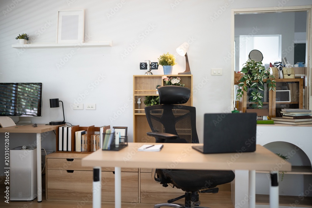 Fototapeta premium A bright, organized home office featuring wooden desks, ergonomic chair, laptop, monitor, and indoor plants, ideal for remote work and productivity concepts