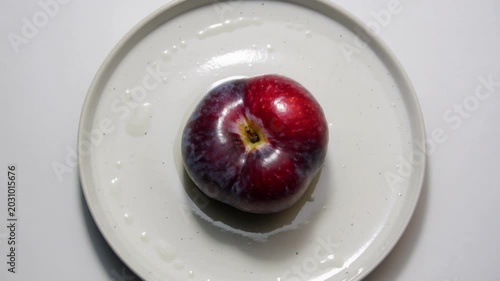 Ripe Purple Plum Rotating on White Ceramic Plate