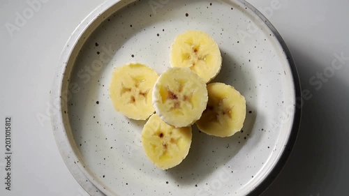 Banana slices being arranged on a rustic ceramic plate top view