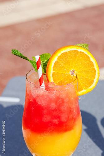 Exotic fruit cocktail with fresh orange garnish close-up in bright sunlight