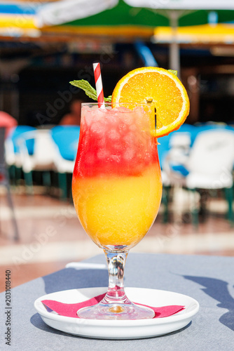 Tropical layered cocktail with orange slice and mint garland on a sunny terrace