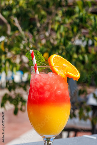 Refreshing orange and strawberry sunrise cocktail in a glass with a straw