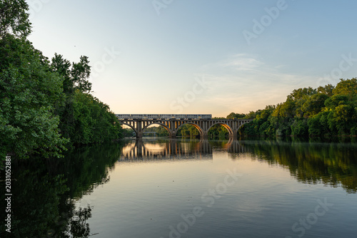 Εκτύπωση καμβά Fredericksburg, Virginia, features an commuter passenger train crossing the historic concrete arch railroad bridge over the calm waters of the Rappahannock River at sunset