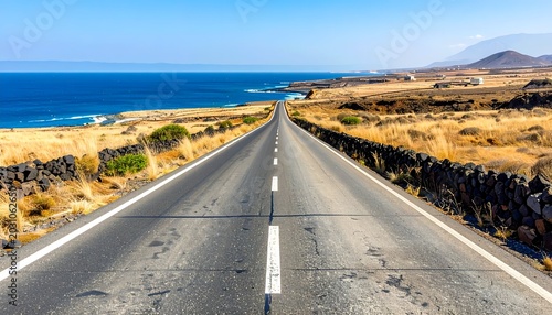 Asphalt road stretches to horizon, bordered by stone walls and sea, under a blue sky