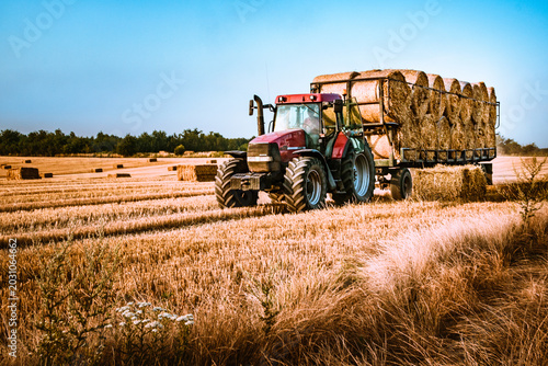 Tableau sur toile Modern red agricultural tractor hauling a large trailer loaded with round hay ba