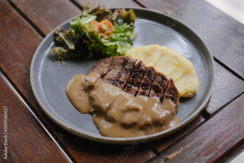 Grilled steak with mushroom sauce, mashed potatoes and salad on plate