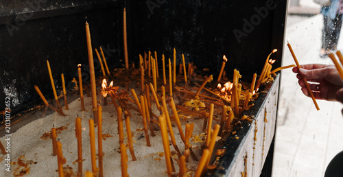 Obraz na plátně Human hand places thin candles into a religious prayer stand