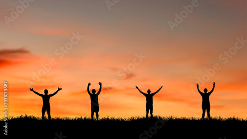 Bild auf Leinwand Four silhouettes of people with arms raised in the air against a vibrant sunset sky