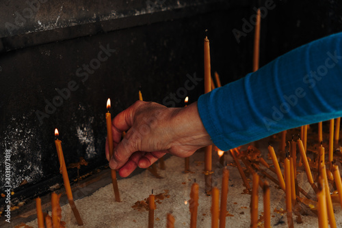 Fotografija Person places a lit candle into white sand inside a religious shrine