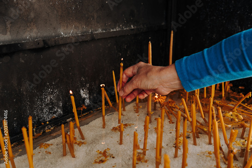 Fotografi Person places a lit candle into white sand inside a religious shrine