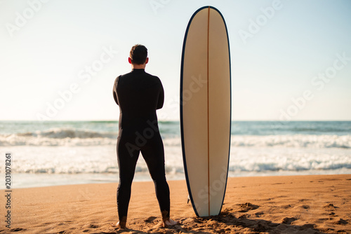 Quadro su tela Surfer wearing wetsuit holding surfboard on beach at sunset