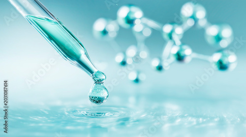 A scientific laboratory research concept using a glass dropper pipette releasing a turquoise drop of liquid onto a glossy surface against a background of blurred glass models of molecules.