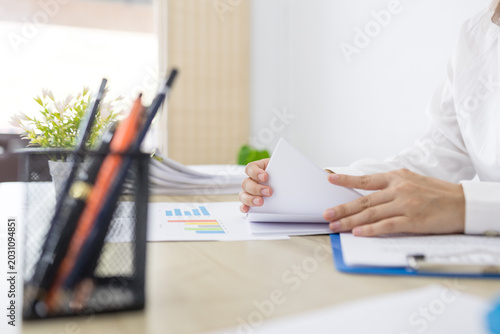 Young woman reviews documents at a bright desk. Focused, she holds a colorful highlighter. Soft natural light fills the minimalist office. Her calm expression suggests careful attention
