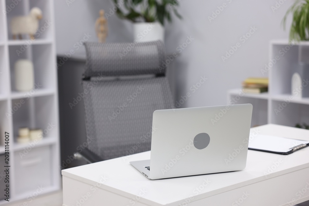 Fototapeta premium White desk with laptop, clipboard, chair and decor in office, closeup