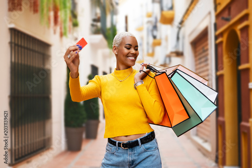 Bild auf Leinwand Happy stylish afro woman with shopping bags and credit card walking in sunny mod