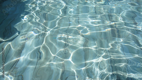 Clear water surface with gentle ripples and reflections. The light creates a shimmering effect on the water, showcasing a tranquil aquatic scene.