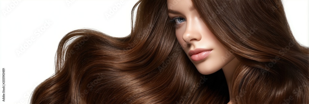 Fototapeta premium A stunning woman with healthy brown wavy hair posing on a white background. Concept of professional hair care, luxury beauty, and silk texture.