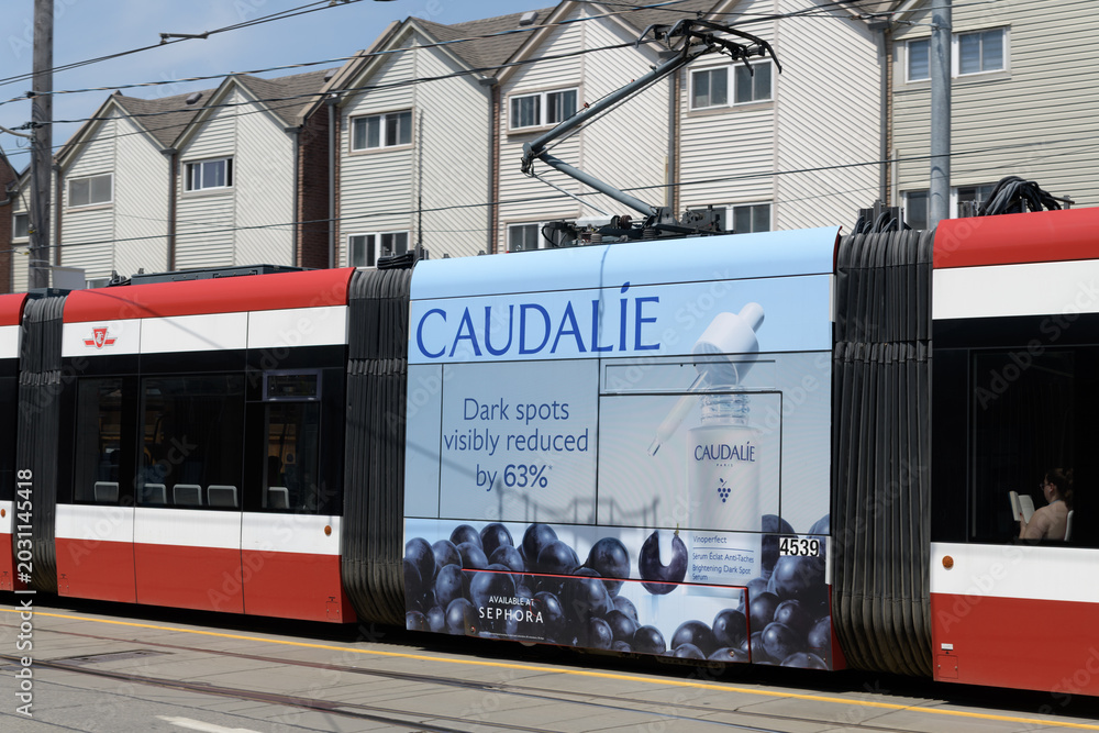 Naklejka premium row housing and trolley advertising wrap for Caudalie, a French skincare brand, on Queen St E, Toronto