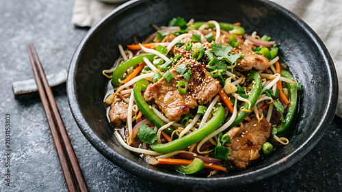 Stir-fried chicken with green beans and noodles in black bowl on dark table with chopsticks