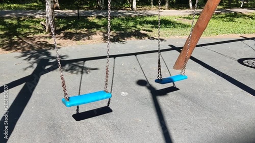 Empty blue swings hanging in a playground with green background  