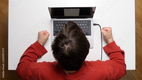 Billede på lærred Young man overwhelmed by work, slamming his forehead on a laptop at a white desk