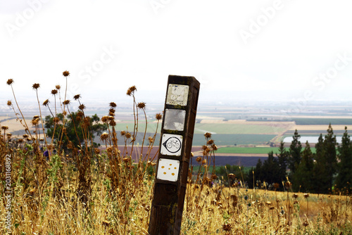 Wooden trail marker with bicycle symbol in dry field overlooking rural landscape