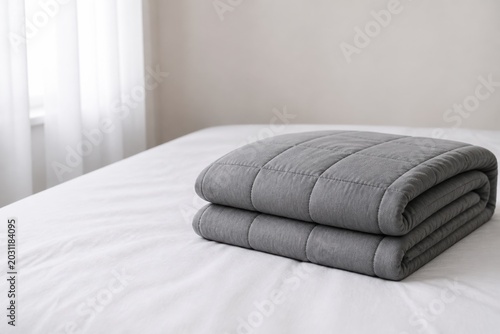 Soft gray blanket folded neatly on a white bed in a bright room with natural light coming through the window
