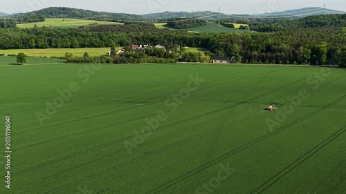 Aerial View of Tractor Working Green Field in Rural Hilly Landscape