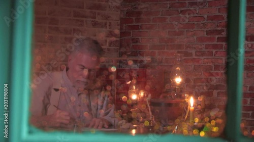 view through a rainy window of a man writing with a dip pen