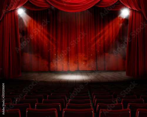 Stage with red curtains, lighting equipment and smoke in front of seats in theater