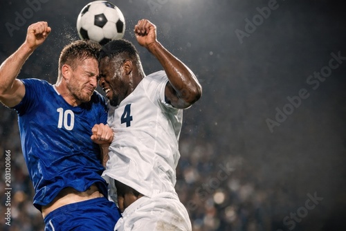 Two Soccer Players Colliding Midair While Competing For Header During Intense Football Match Under Stadium Lights. Powerful Sports Action Scene Showing Physical Aerial Duel And Competitive Game Energy