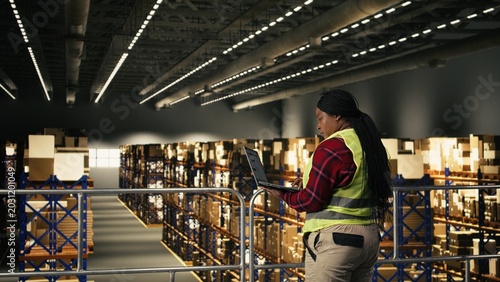 Quadro su tela African American worker, shipping and delivery, process using laptop, warehouse facility